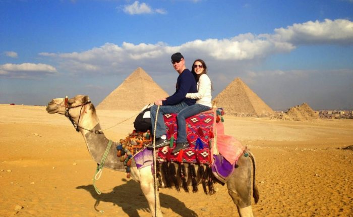 Couple riding a decorated camel in the desert in front of the Giza Pyramids