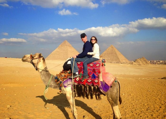 Couple riding a decorated camel in the desert in front of the Giza Pyramids