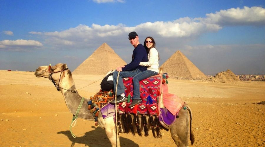 Couple riding a decorated camel in the desert in front of the Giza Pyramids