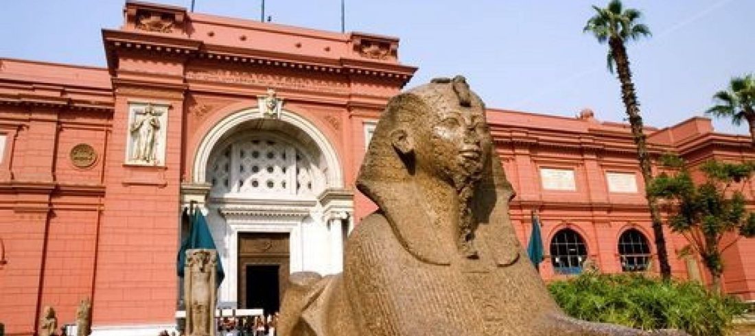 Red facade of the Egyptian Museum in Tahrir Square, Cairo, with a sphinx statue in the garden
