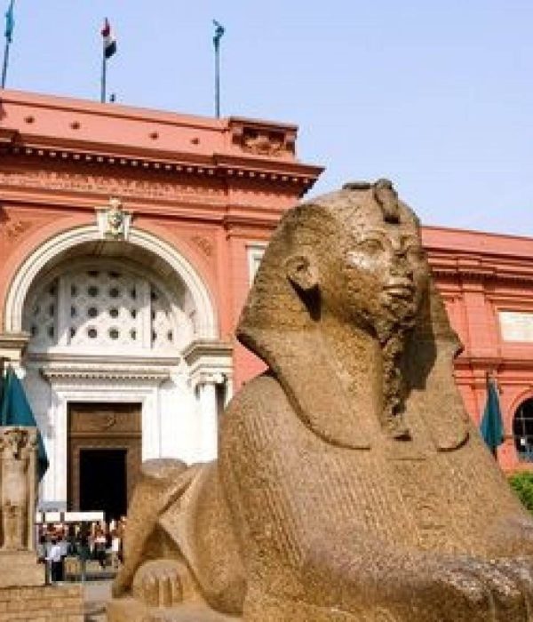 Red facade of the Egyptian Museum in Tahrir Square, Cairo, with a sphinx statue in the garden
