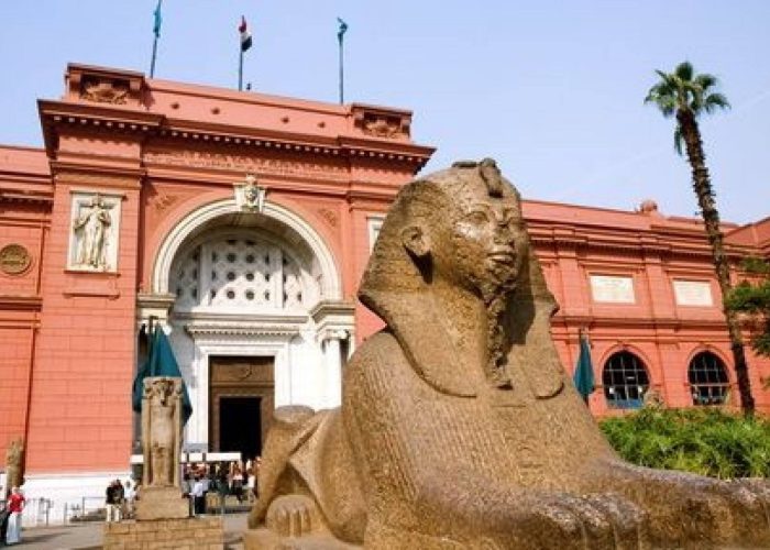 Red facade of the Egyptian Museum in Tahrir Square, Cairo, with a sphinx statue in the garden