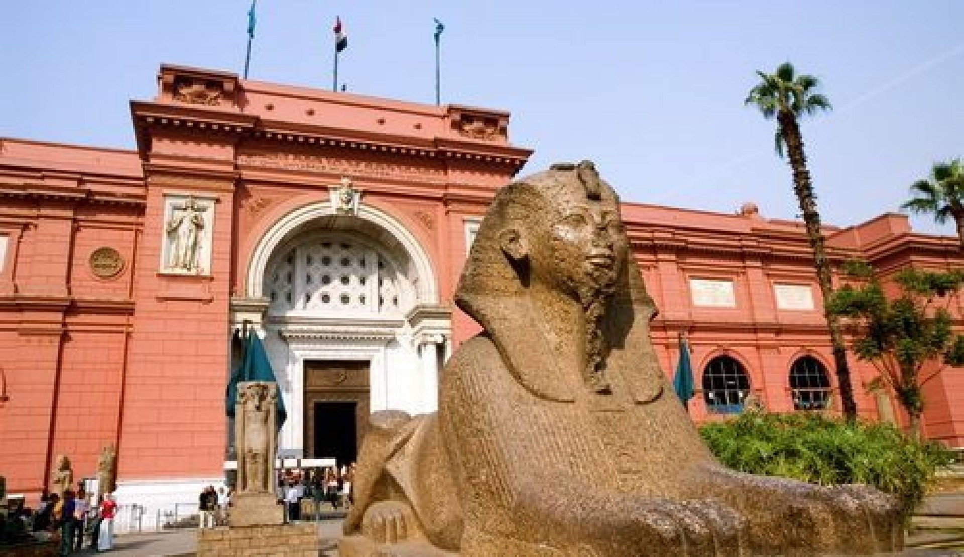 Red facade of the Egyptian Museum in Tahrir Square, Cairo, with a sphinx statue in the garden