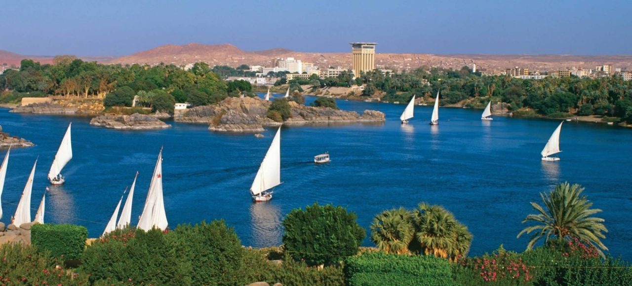 White-sailed feluccas on the Nile in Aswan with the West Bank hills behind