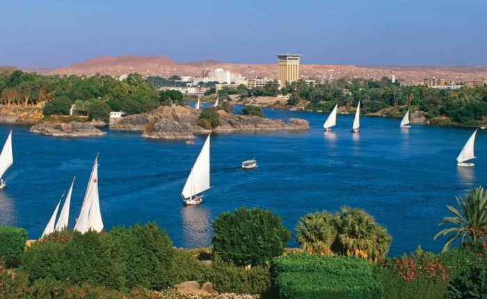White-sailed feluccas on the Nile in Aswan with the West Bank hills behind