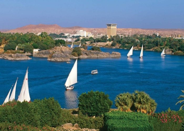 White-sailed feluccas on the Nile in Aswan with the West Bank hills behind