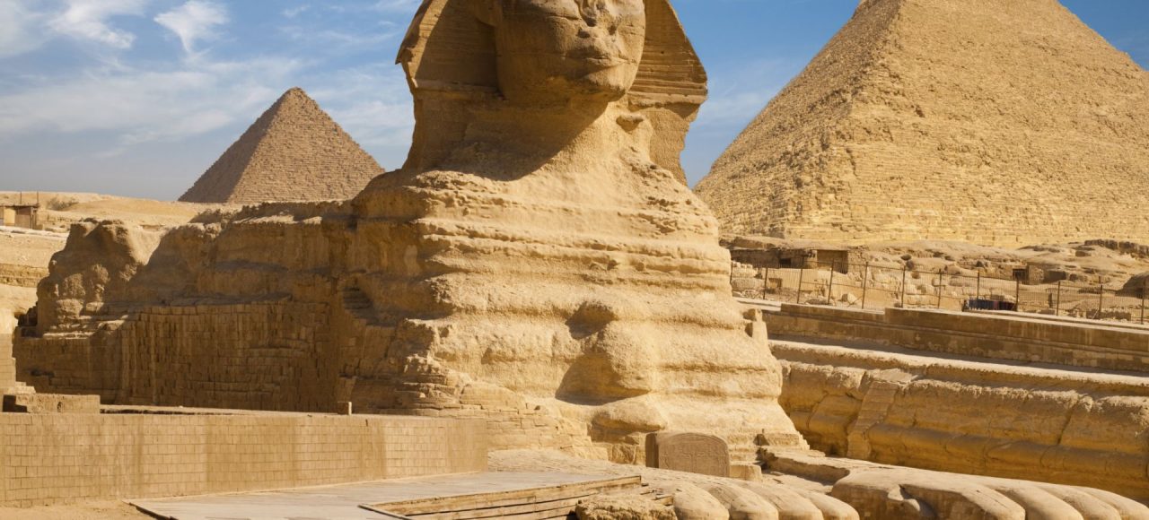 The Great Sphinx of Giza with the pyramids of Khafre and Khufu under a blue sky