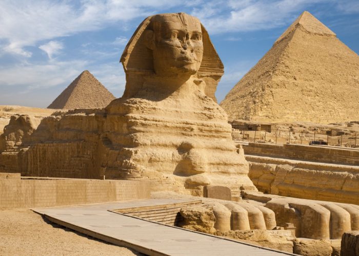 The Great Sphinx of Giza with the pyramids of Khafre and Khufu under a blue sky