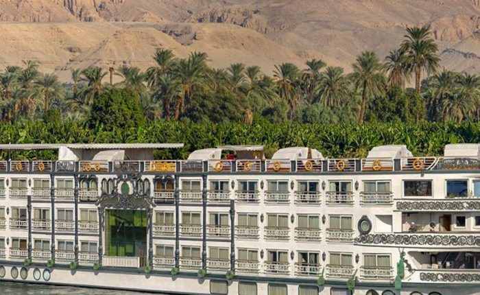 Nile cruise ship sailing past palm trees and mountains, Egypt