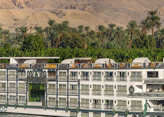 Nile cruise ship sailing past palm trees and mountains, Egypt