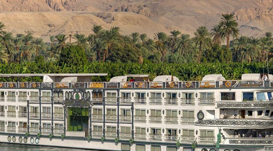 Nile cruise ship sailing past palm trees and mountains, Egypt