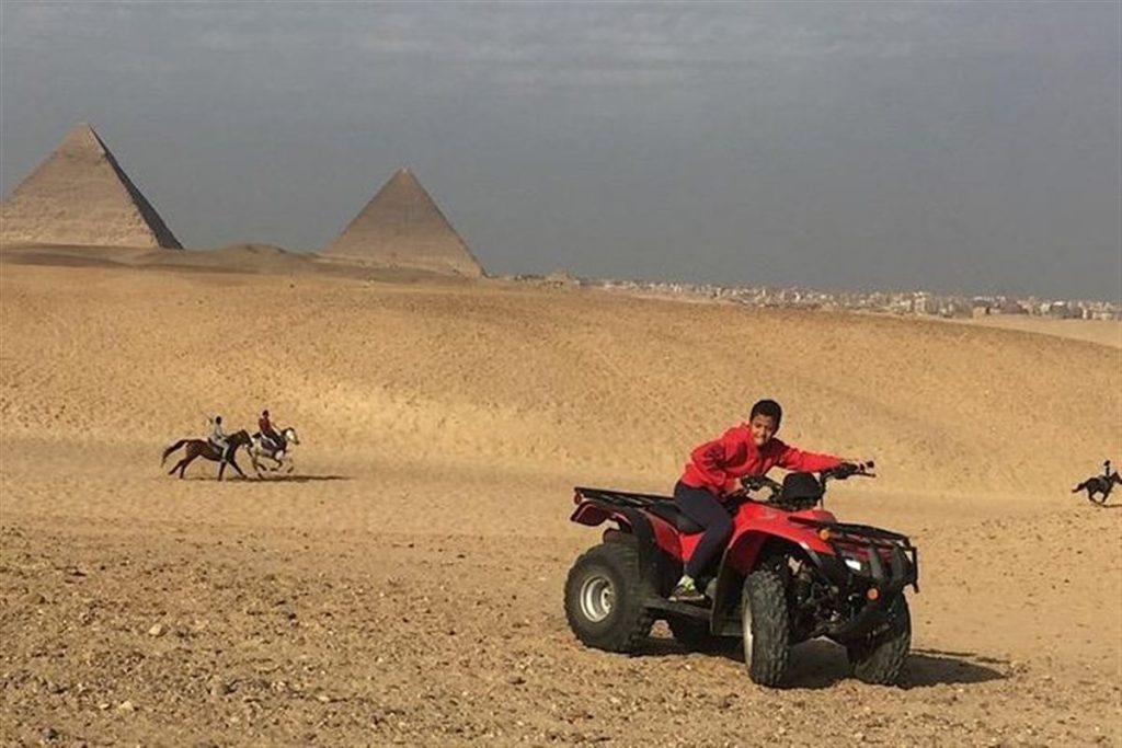 Quad bike rider in the desert with the Giza Pyramids behind