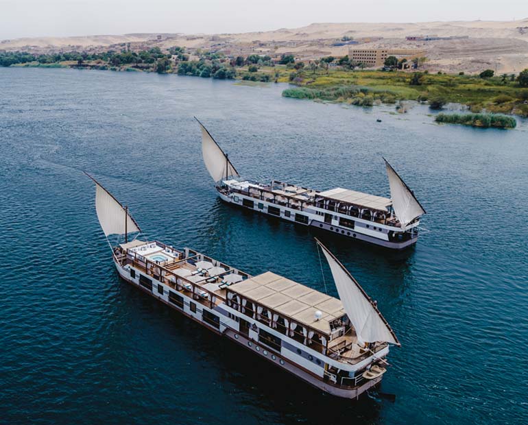 Two dahabiya boats with white sails on the Nile near Aswan