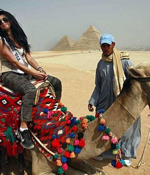 Smiling traveller on a camel led by a local guide at the Giza Pyramids